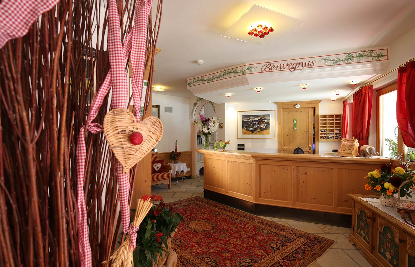 La reception dell'Hotel Mesdì arredata in legno, con fiori sul bancone e un tappeto sul pavimento