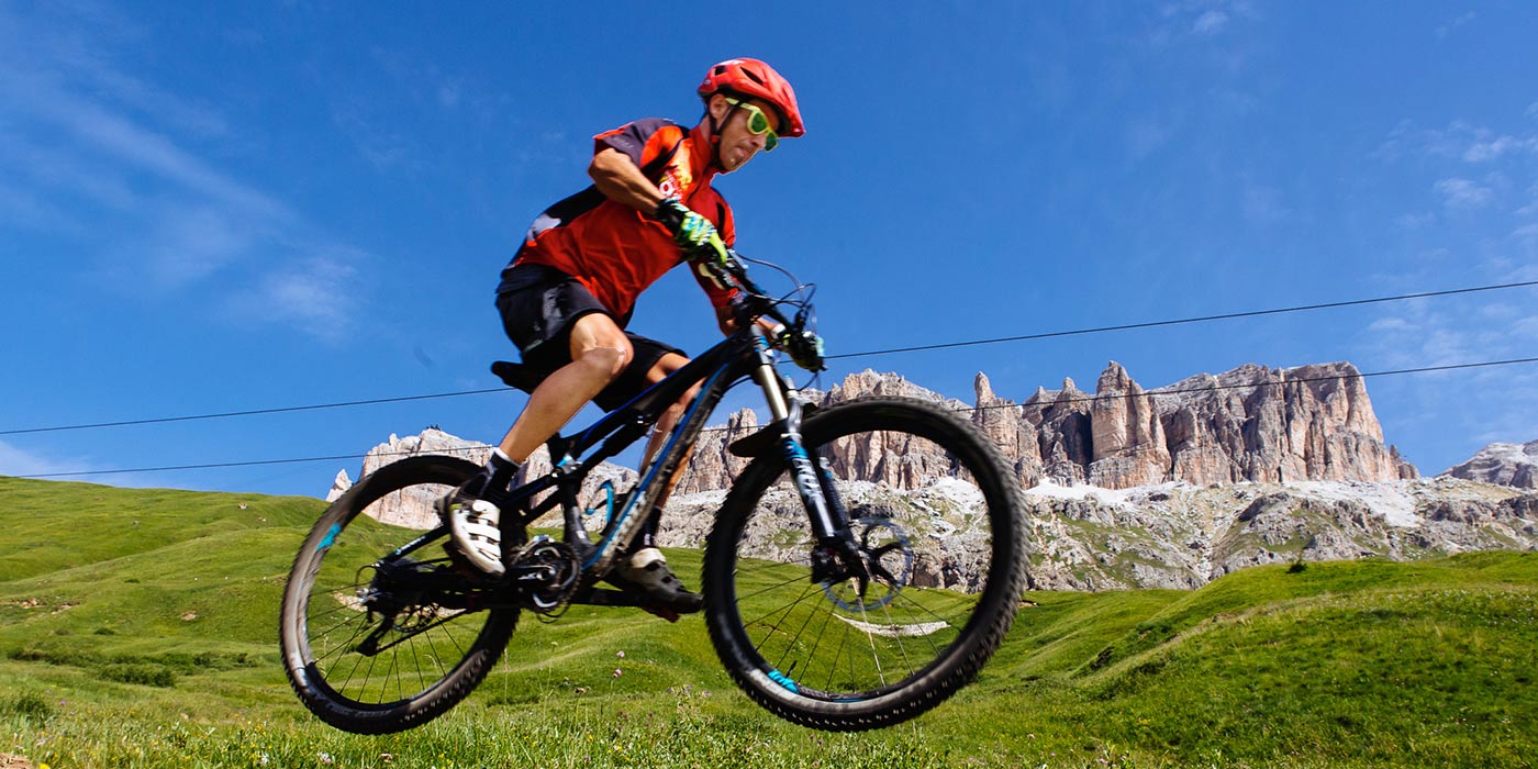 Man in mountain bike on a green meadow with the Dolomites on the background