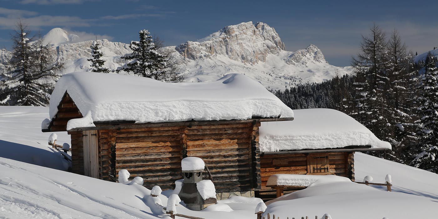 Baita di legno in inverno coperta di neve con le Dolomiti innevate sullo sfondo
