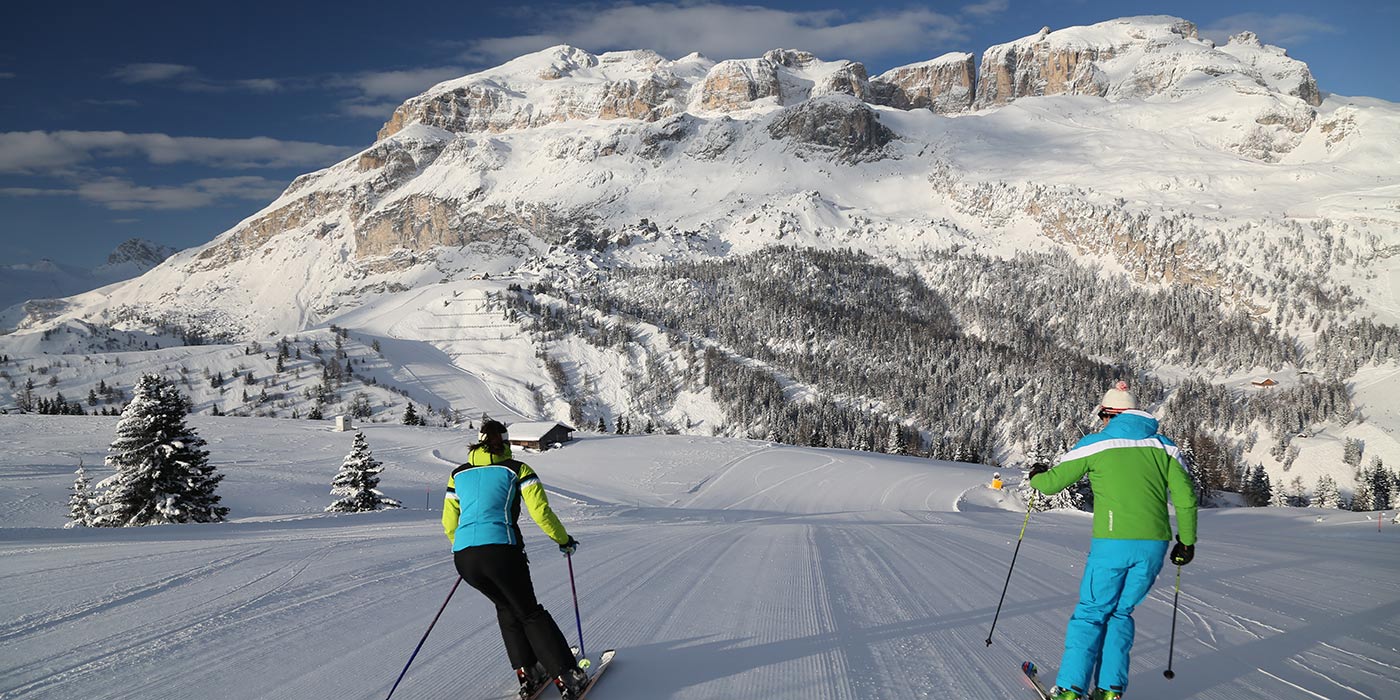 Coppia di sciatori lungo una pista con le Dolomiti sullo sfondo