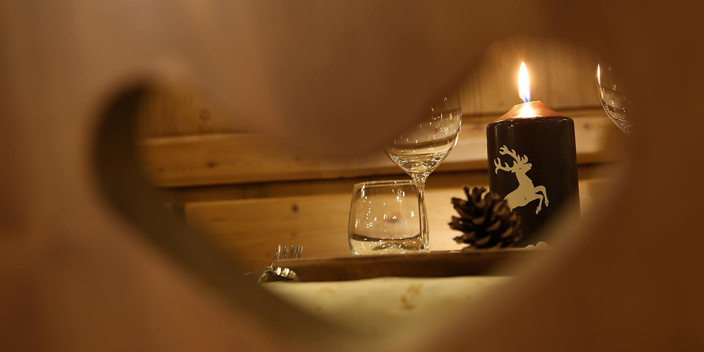 Gedeckter Tisch mit brennender Kerze, durch die Lehne eines Holzstuhles gesehen