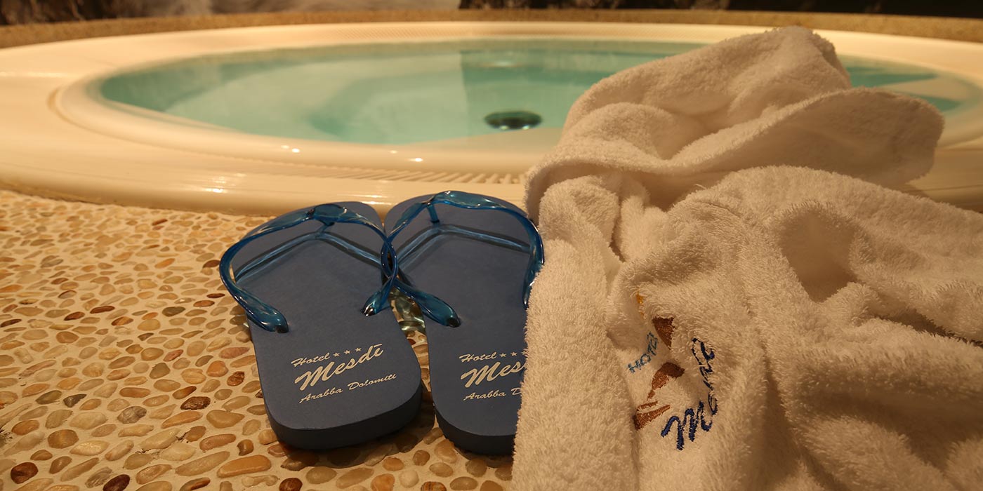 Schwarze Badeschlappen und ein weißer Bademantel auf dem Rand des Whirlpools des Hotels Mesdì
