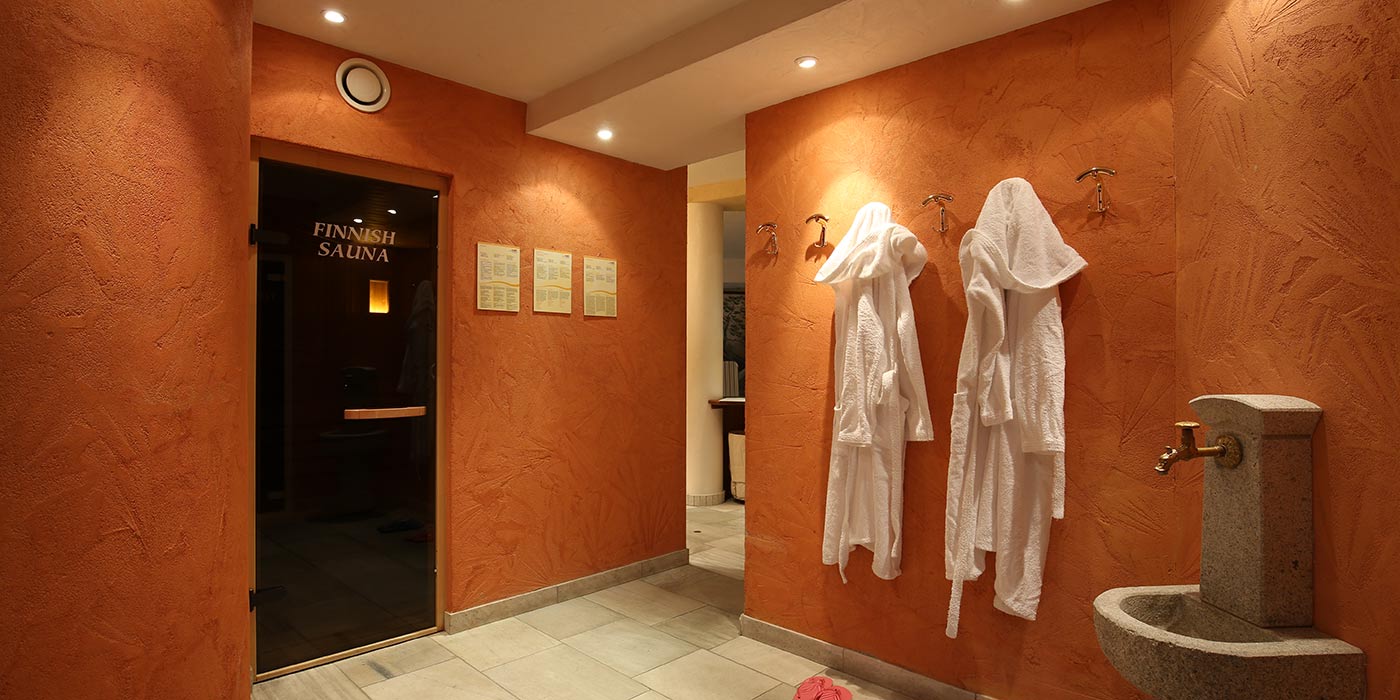 L'accesso della sauna finlandese dell'Hotel Mesdì con fontanella di pietra e accappatoi appesi alla parete