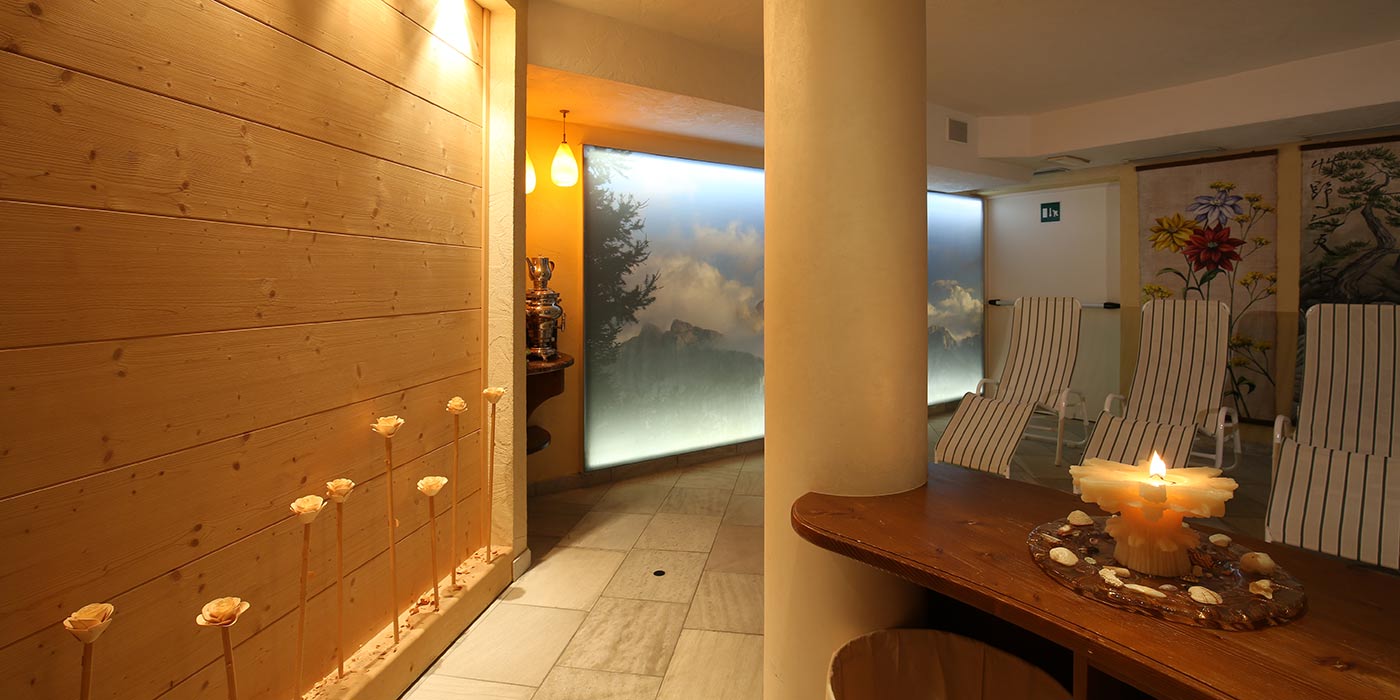 L'area wellness dell'Hotel Mesdì arredatata in legno con una candela accesa sul tavolo e lettini lungo la parete