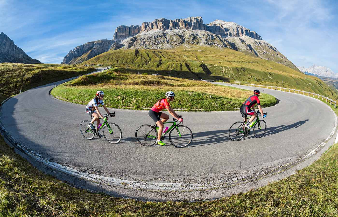 Uomo in mountain bike su una strada sterrata con prati verdi, impianti di risalita e Dolomiti sullo sfondo