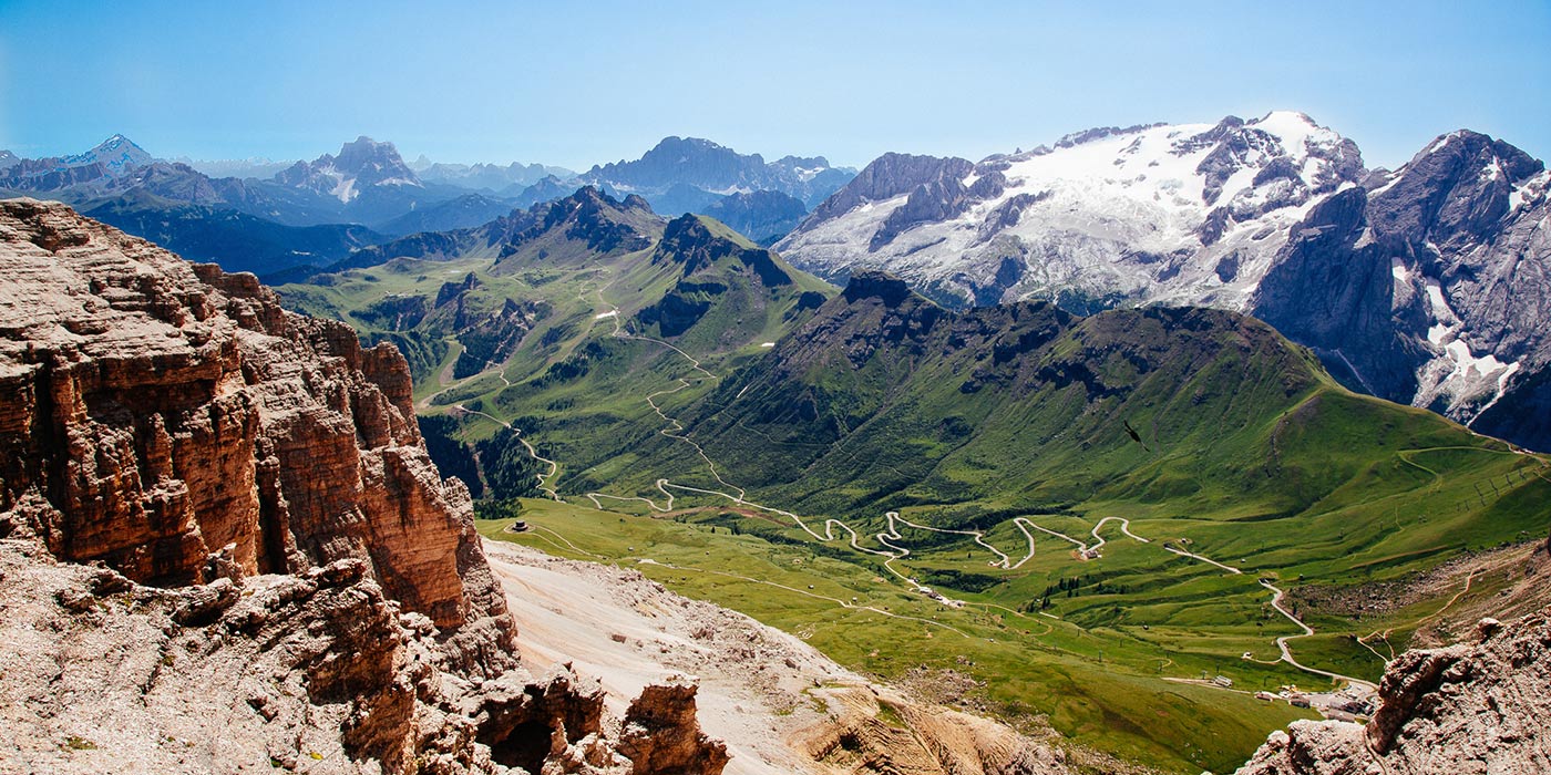 Passo Pordoi's street descends towards Arabba in summer with the Dolomites on the background