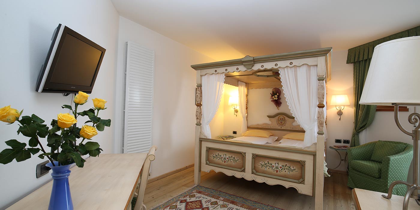 Room with canopy bed, green chair and yellow flowers vase on the desk