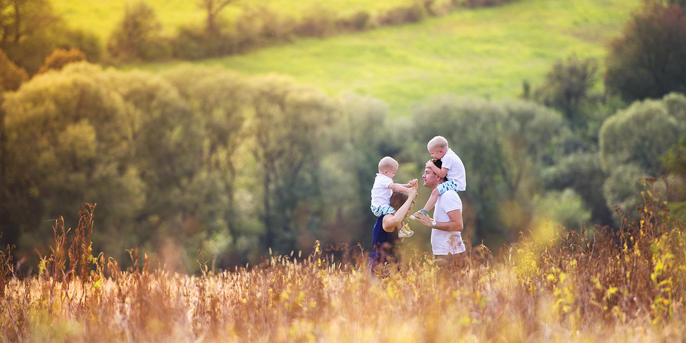 Famiglia in mezzo a un prato autunnale con prati verdi e alberi sullo sfondo